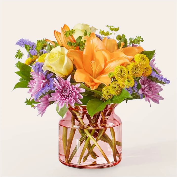 Orange lilies and mixed flowers in a pink glass vase