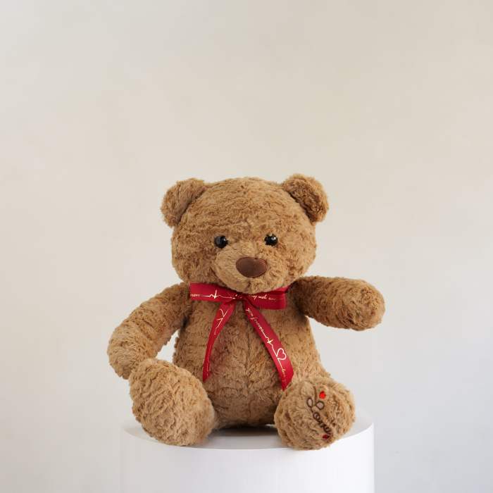 Brown teddy bear with a red ribbon sitting on a white pedestal