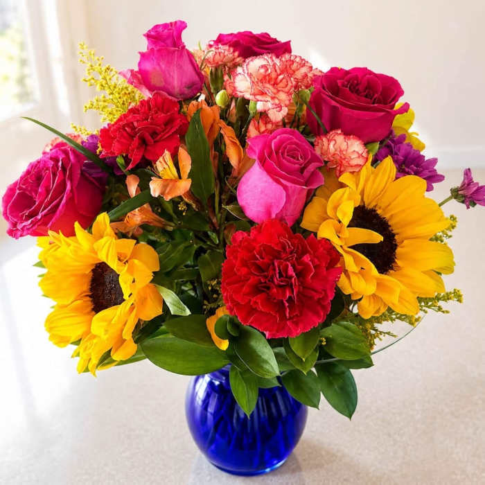 Mixed bouquet of roses, sunflowers, and carnations in a blue glass vase