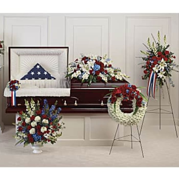 Patriotic funeral floral set with red, white, and blue arrangements around a casket