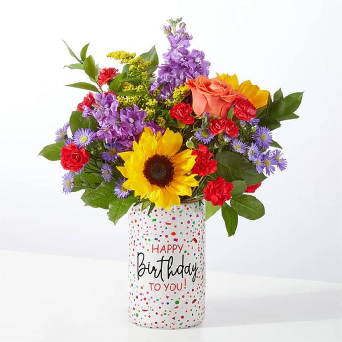Mixed bouquet in a birthday vase with a sunflower, roses, and purple blooms