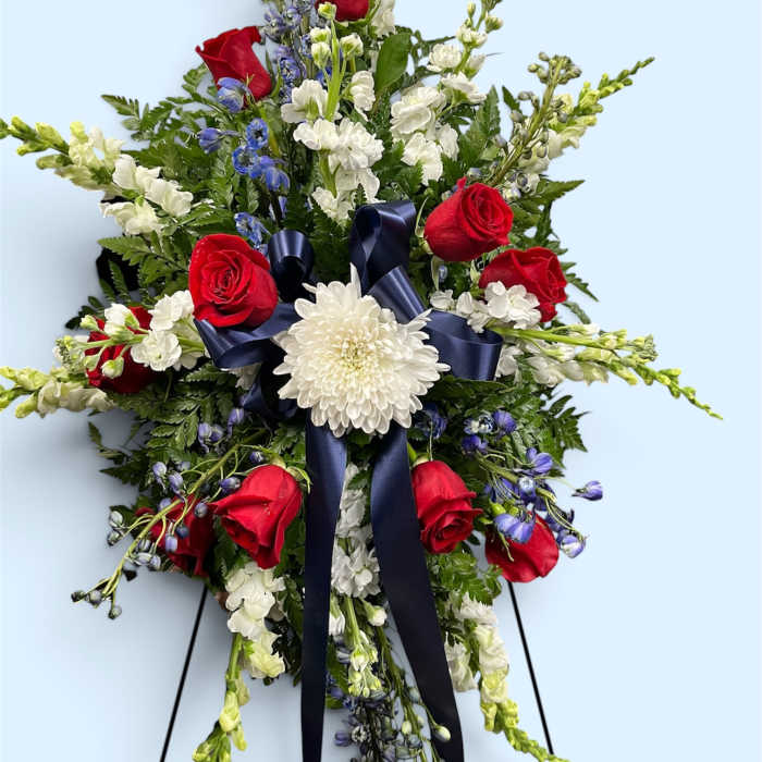 Standing floral spray with red roses, white blooms, and a navy ribbon