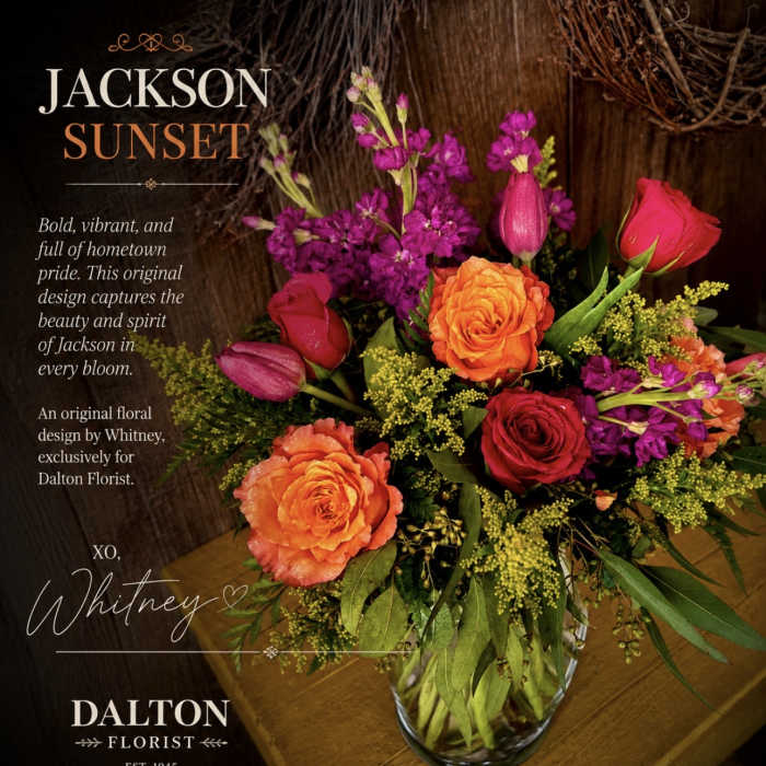 Mixed bouquet of orange and red roses with purple blooms in a glass vase