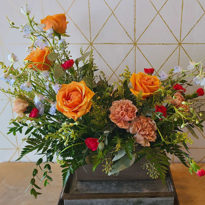 Mixed bouquet with orange roses, peach carnations, and white blossoms in a rectangular container