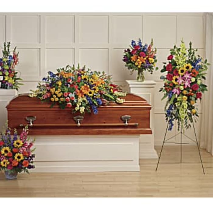 Colorful funeral floral sprays surround a wooden casket in a chapel.