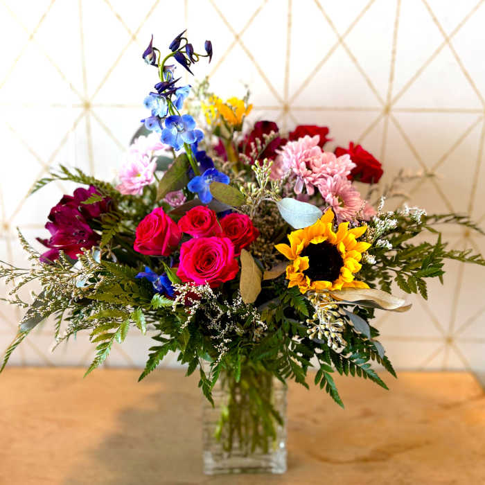 Mixed bouquet with roses, sunflowers, and blue flowers in a glass vase