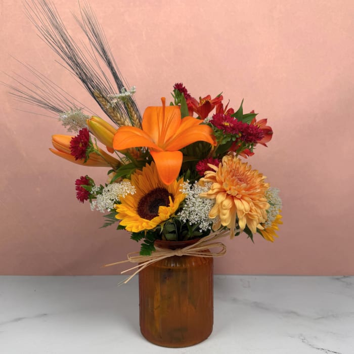 Orange and yellow flower arrangement in an amber glass vase