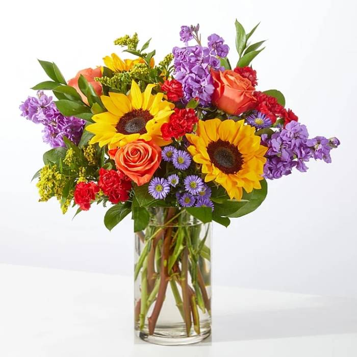 Mixed bouquet with sunflowers, roses, and purple flowers in a glass vase