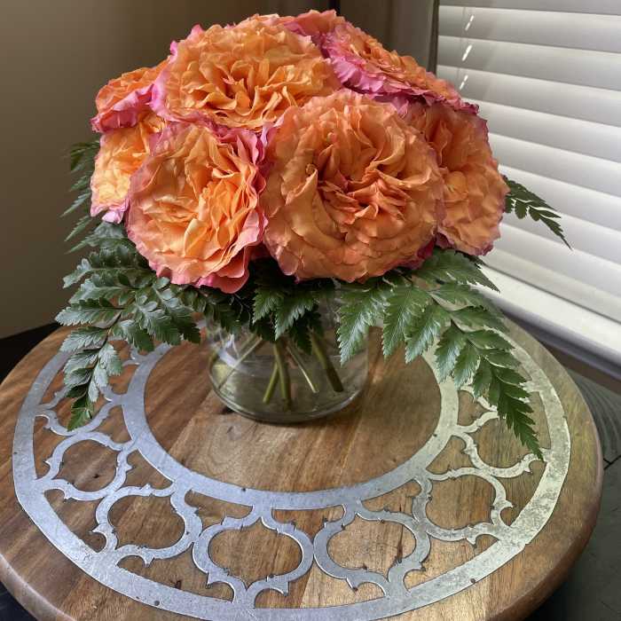 Orange and pink roses in a clear glass vase with fern foliage