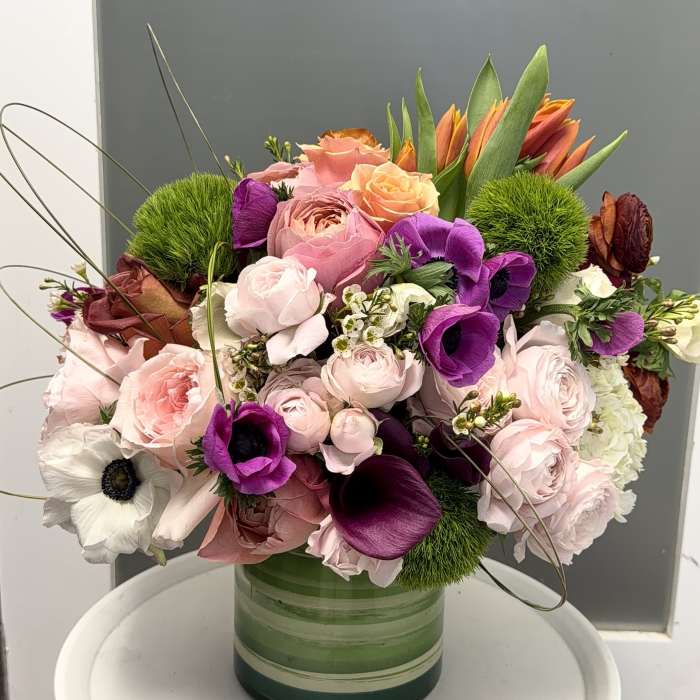 Mixed pink, purple, and orange flowers arranged in a green glass vase.
