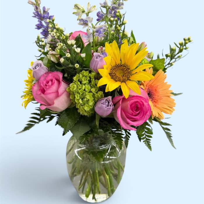 Mixed bouquet of pink roses, sunflowers, and purple flowers in a glass vase