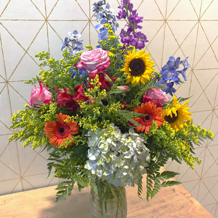 Mixed bouquet in a glass vase with roses, sunflowers, hydrangea, and blue-purple blooms