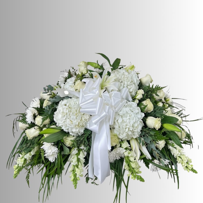 White floral spray with lilies, roses, and hydrangeas tied with a white ribbon