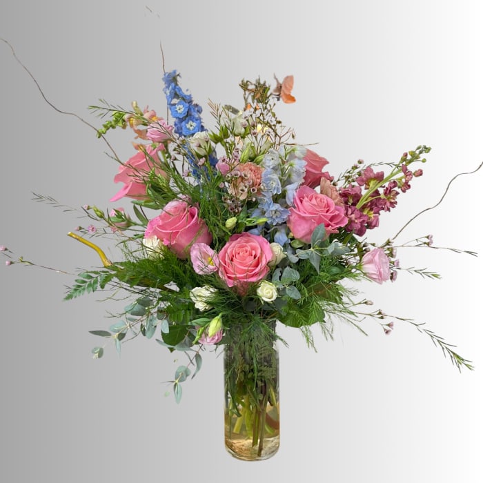 Tall mixed bouquet of pink and blue flowers in a clear glass vase