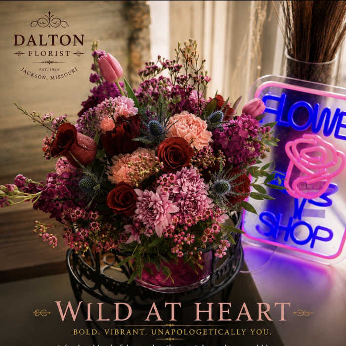 Mixed bouquet of pink and red flowers in a vase beside a neon flower shop sign
