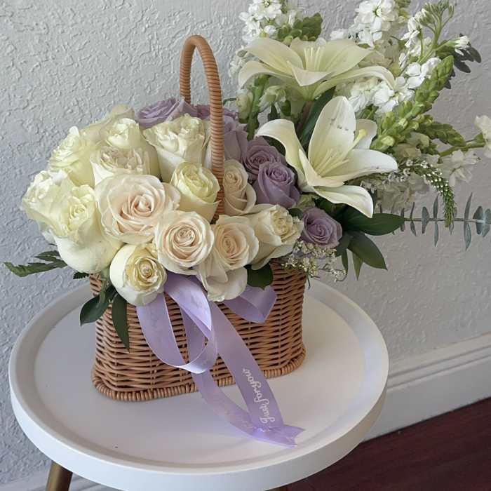 Basket of cream and lavender roses with white lilies and ribbon