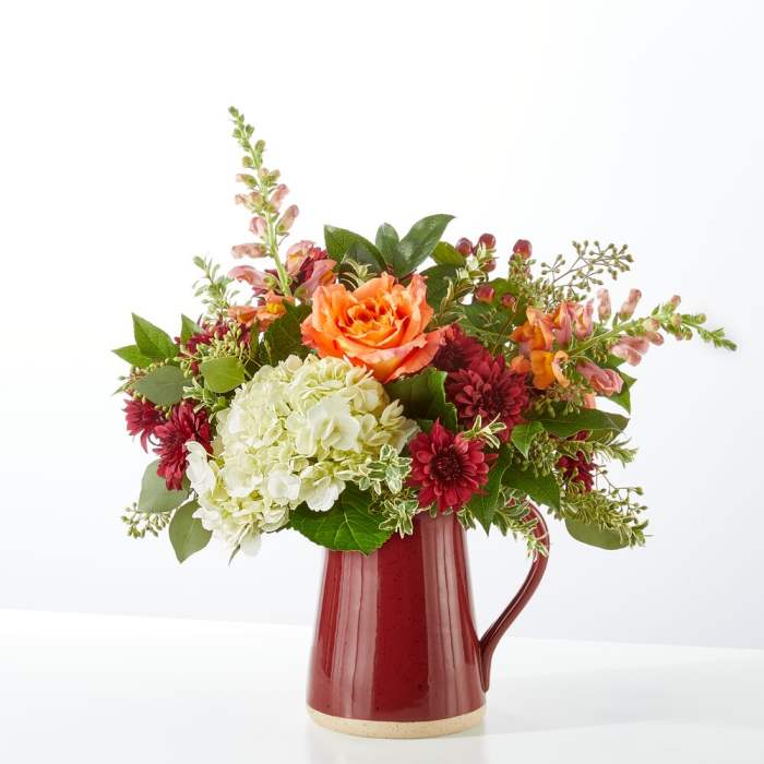 Mixed bouquet in a red ceramic pitcher with orange, white, and burgundy flowers