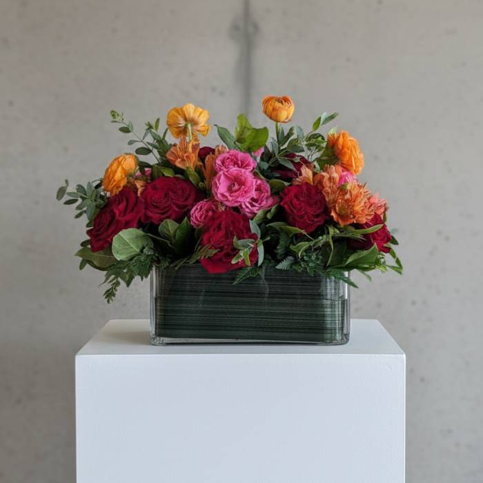 Mixed bouquet of red, pink, and orange flowers in a rectangular glass vase