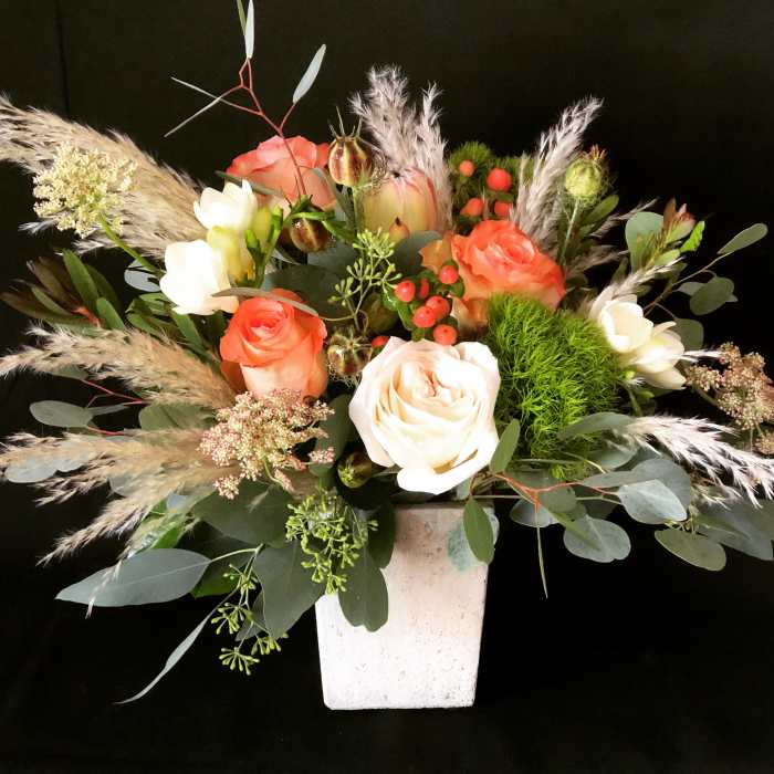 Mixed rose arrangement in a white square vase with airy grasses