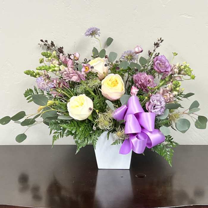 Pastel floral arrangement in a white vase with a purple ribbon