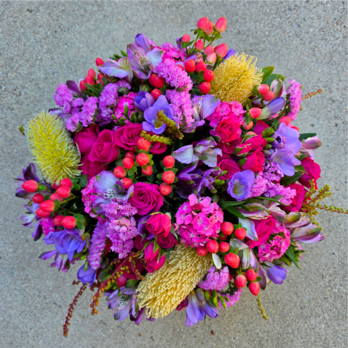 Round bouquet of pink, purple, and yellow flowers on a gray surface