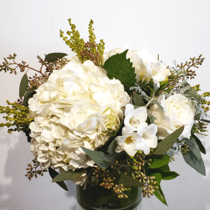 White hydrangeas and roses in a glass vase with mixed greenery