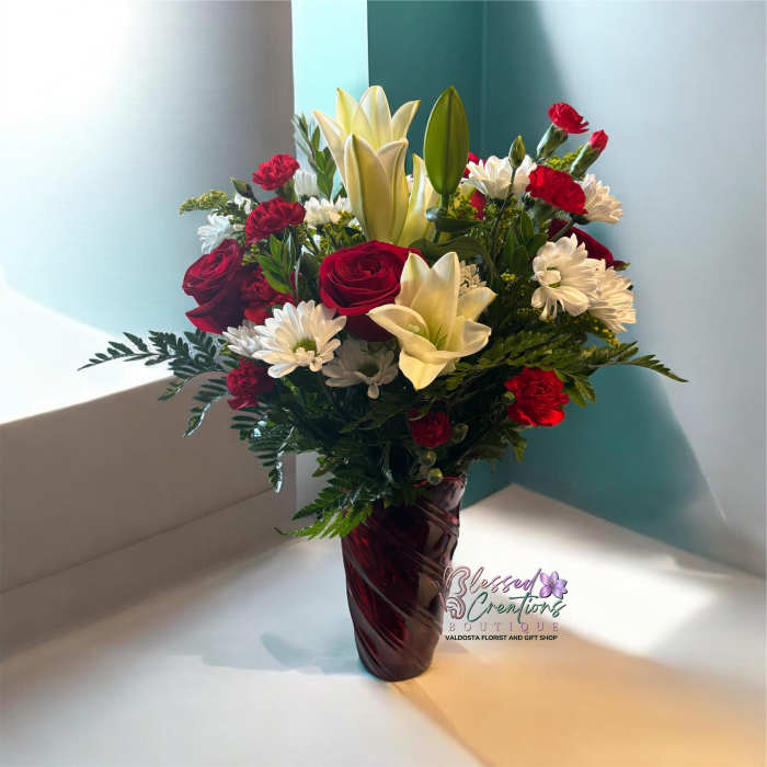 Bouquet of red roses, white lilies, and white daisies in a burgundy vase