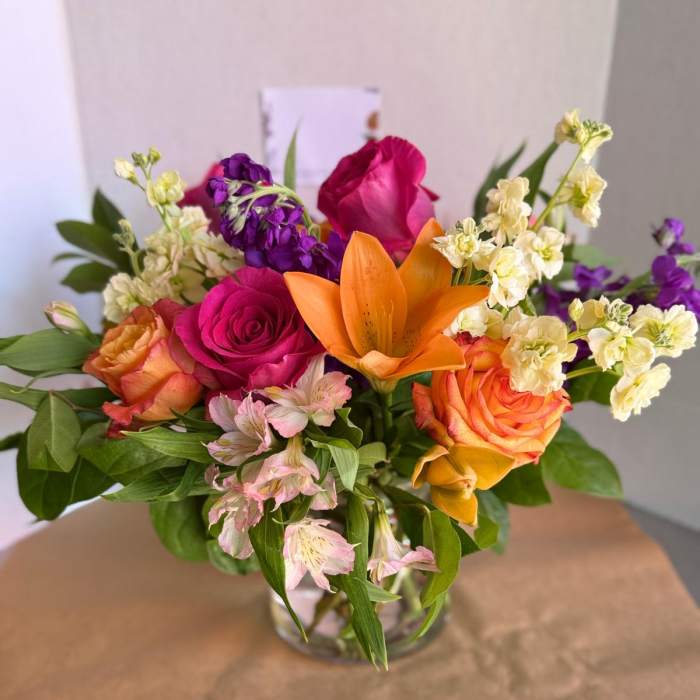 Mixed bouquet of roses, lilies, and purple blooms in a glass vase