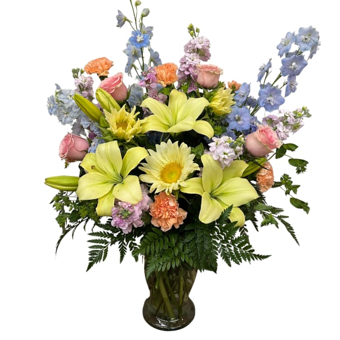 Mixed bouquet of lilies, roses, and blue flowers in a glass vase