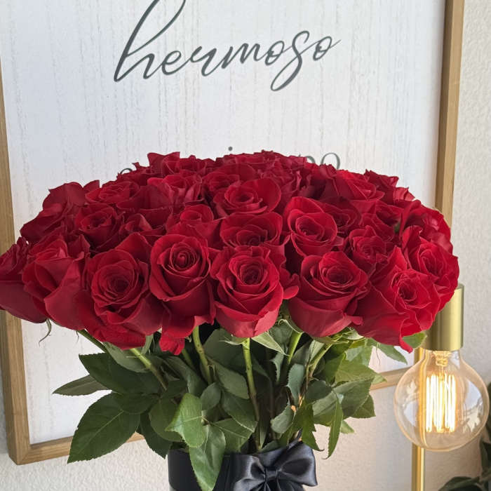 A tall vase of red roses tied with a black ribbon
