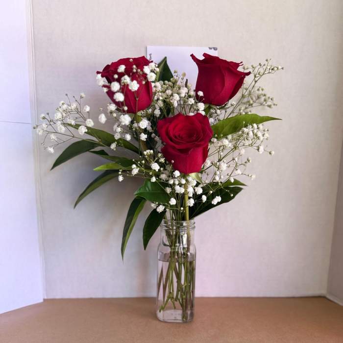 Three red roses in a clear glass vase with white baby's breath