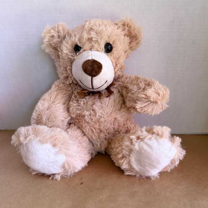 Plush teddy bear with a brown ribbon sitting against a plain background
