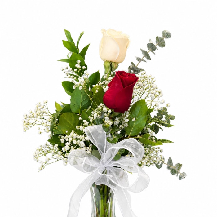 Red and white roses in a clear glass vase with a white ribbon