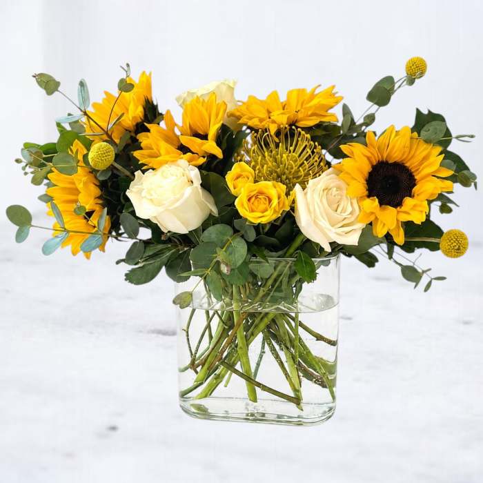 Yellow sunflowers and white roses arranged in a clear glass vase