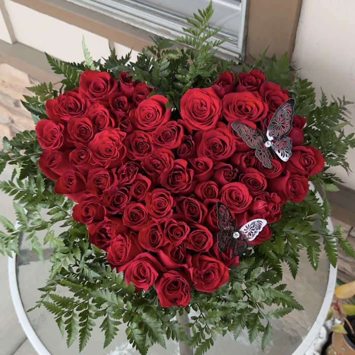 Heart-shaped bouquet of red roses with fern-like greenery and butterfly accents