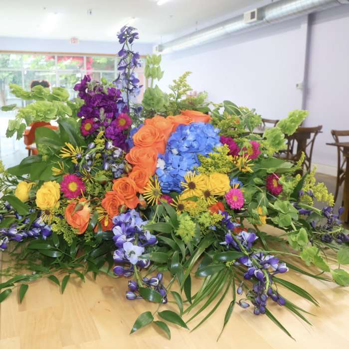 Large colorful floral arrangement with roses, hydrangeas, and purple blooms on a table