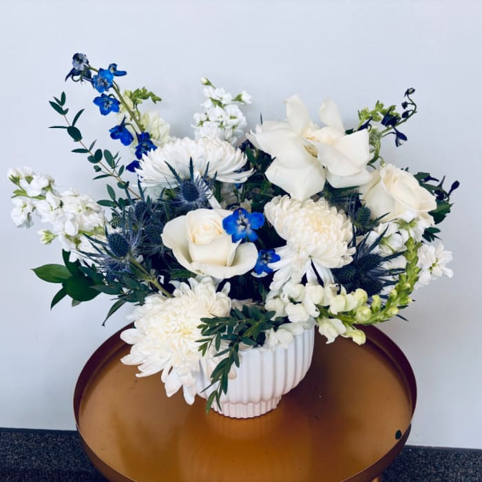 White and blue floral arrangement in a ribbed white vase