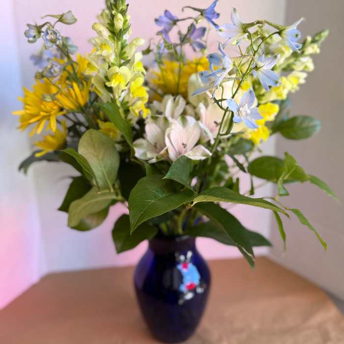Mixed bouquet of yellow, blue, and pale pink flowers in a dark vase