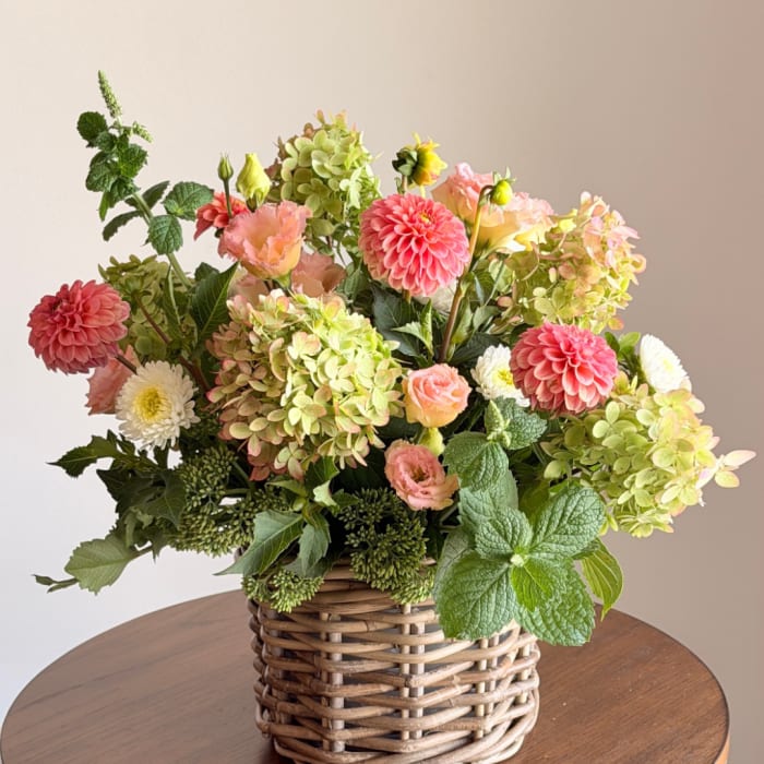Mixed floral arrangement in a woven basket with pink, peach, white, and green blooms