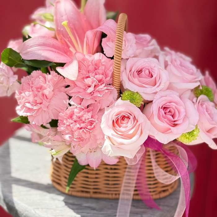 Pink roses and carnations in a wicker basket with ribbon