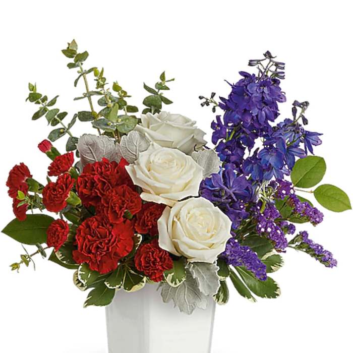 Red and white roses with purple flowers in a clear square vase