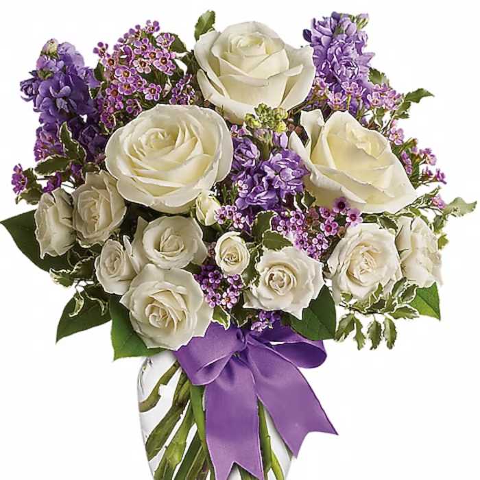 White roses and purple flowers arranged in a glass vase with a purple ribbon