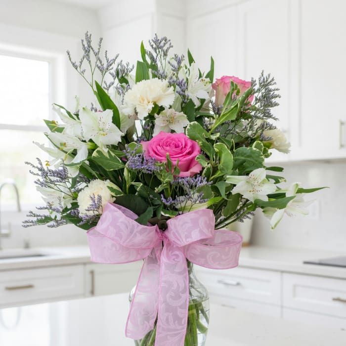 Pink rose bouquet with white flowers in a glass vase and pink ribbon