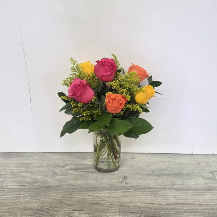 Bright bouquet of pink, yellow, and orange roses with yellow filler in a clear glass vase