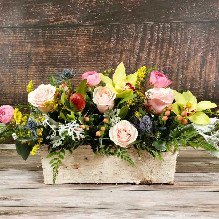 Low floral arrangement with pink roses and yellow orchids in a rustic white container