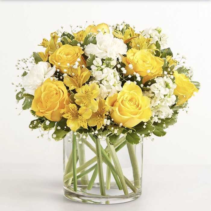 Yellow roses and white flowers arranged in a clear glass vase.