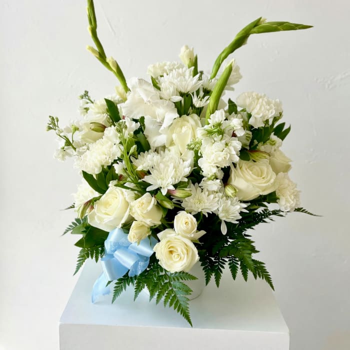 White roses and chrysanthemums arranged in a vase with a blue ribbon