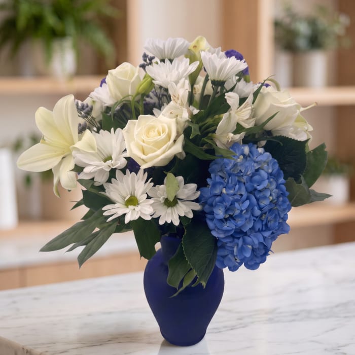 White and blue mixed bouquet in a dark blue vase