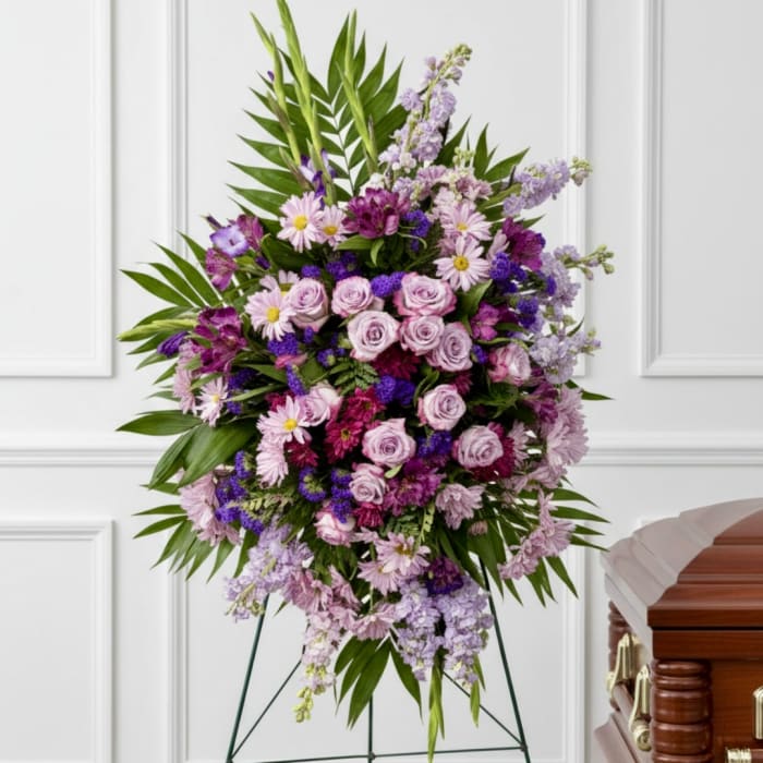 Large purple and pink floral standing spray beside a casket