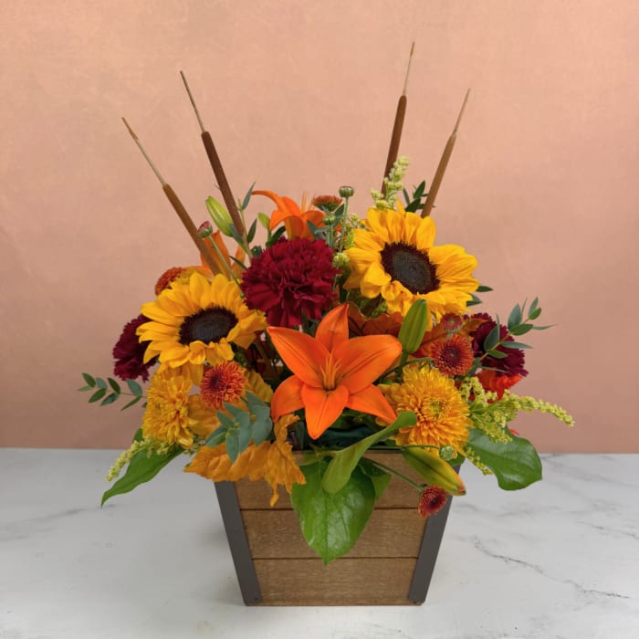 Autumn flower arrangement with sunflowers, lilies, and mums in a wooden planter